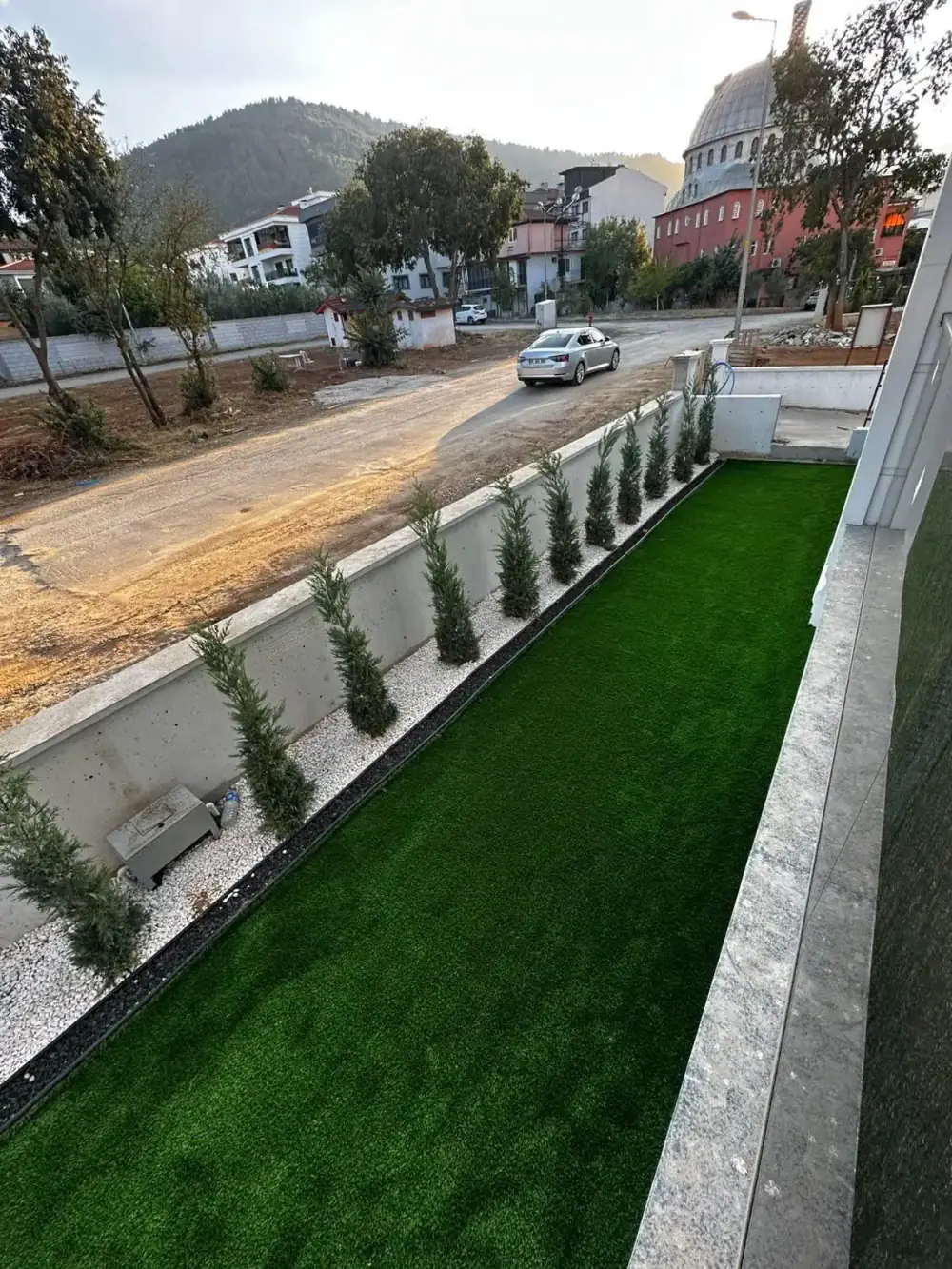 Servi sırası ve beyaz taşlı bordürle çevrili çim alan